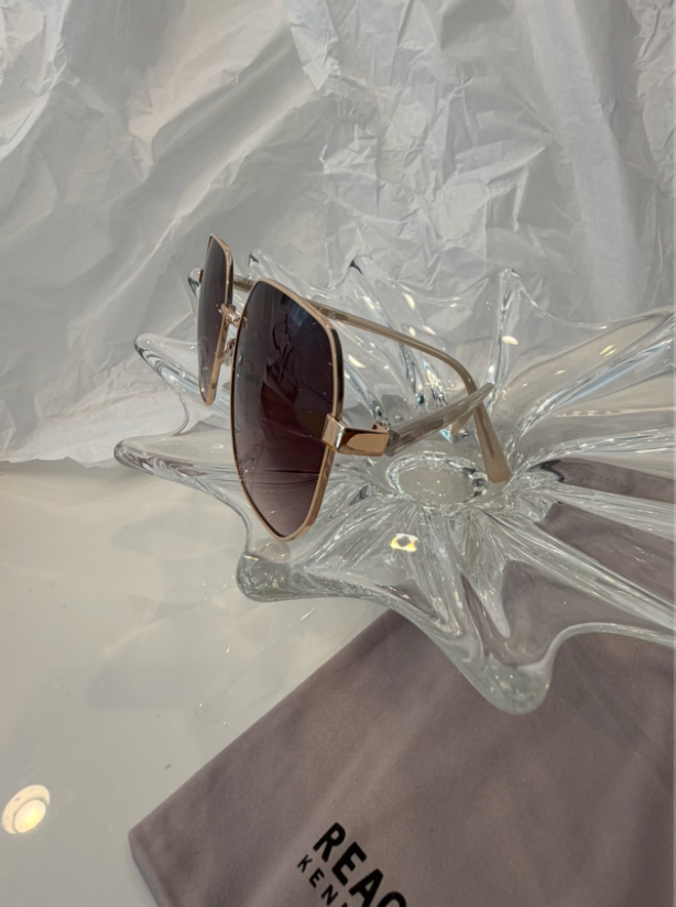 Kenneth Cole Reaction KC3002 gold geometric sunglasses front view on crystal display