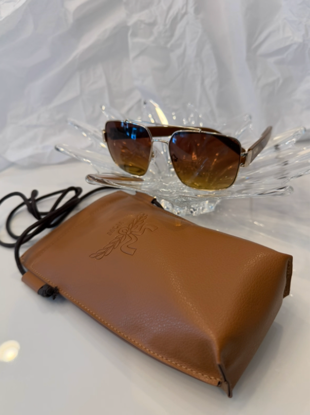 MCM MW0008 gold square aviator sunglasses front view with original MCM tan leather drawstring case on crystal display